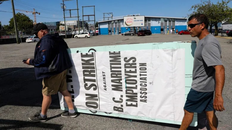 Port workers with the International Longshore and Warehouse Union Canada remove a strike sign from a picket line outside the despatch hall in Vancouver on July 13