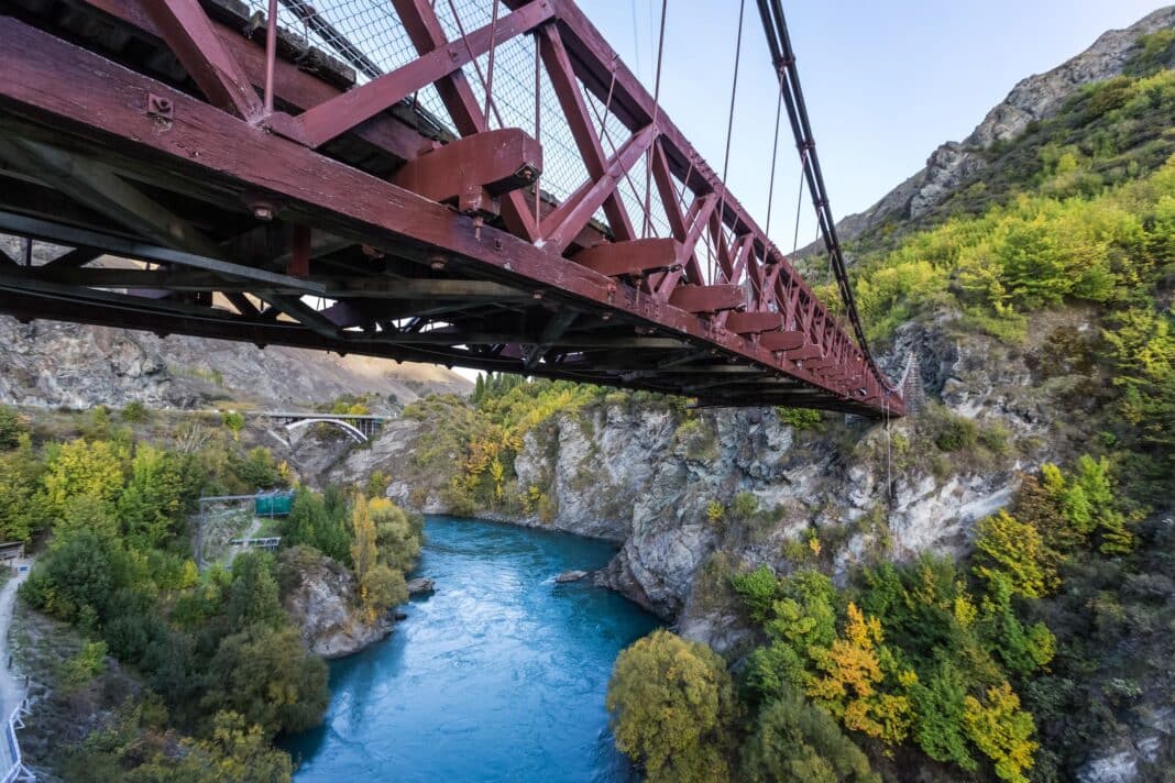 The Kawarau Gorge Suspension Bridge spans the Kawarau River in the Otago region of the South Island of New Zealand. The historic timber bridge is mainly used for commercial purposes by the AJ Hackett Bungy Company, making it the world’s first commercial bungy jumping site. Additionally, the bridge serves as a crossing point for walkers, runners, and bikers on the Queenstown Trail. (Photo Credit: Dreamstime)