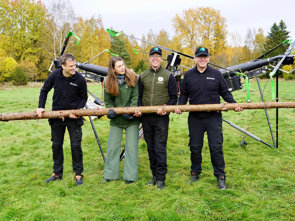 Four members of the AirForestry team holding a felled tree trunk in front of the company's harvesting drone.