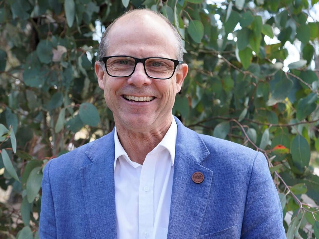 Australian Forest Products Association acting chief executive Richard Hyett in a blue jacket standing in front of eucalyptus foliage