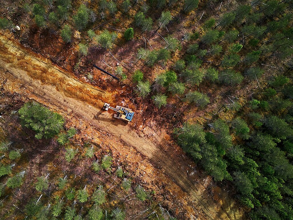 Aerial view of an excavator on a dirt track cut through a Finnish pine forest